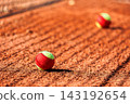 clay tennis court with scattered two-tone balls under bright sunlight. The net and long shadows create a dynamic atmosphere, emphasizing movement and competition 143192654