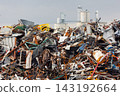Massive concrete silos tower behind piles of scattered scrap metal and industrial debris. Scene shows impact of heavy manufacturing on fragile environment, urging sustainable waste solutions 143192664