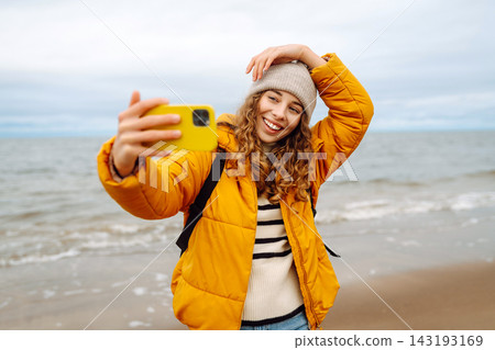 Young tourist woman takes a selfie or blogs on the seashore, enjoying sea scenery. Trips, weekend. Young tourist woman takes a selfie or blogs on the seashore, enjoying sea scenery. Trips, weekend. 143193169