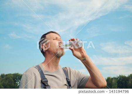 Man hydrating and quenching thirst under blue sky on warm day Man hydrating and quenching thirst under blue sky on warm day 143194796
