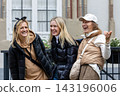 Cheerful friends laugh together on autumn city walk, sharing hugs and joyful travel moments. Candid group portrait captures friendship, reunion, happiness, leisure and weekend adventure outdoors 143196006