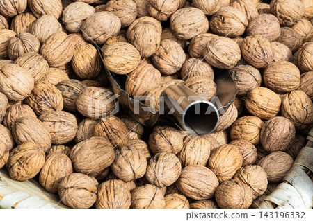 Pile of whole walnuts in shells inside a wicker basket with a metal scoop 143196332