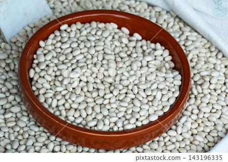 Dry white navy beans filling a brown ceramic bowl on a rustic market display Dry white navy beans filling a brown ceramic bowl on a rustic market display 143196335