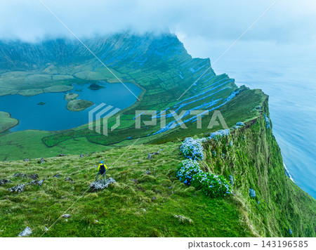 Aerial view of hiker by hydrangeas on Corvo Island cliff overlooking Caldeirao Aerial view of hiker by hydrangeas on Corvo Island cliff overlooking Caldeirao 143196585