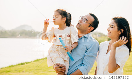 Asian family having fun playing together on spring meadow field grass in park, Happy parents father carrying daughter and a child blowing soap bubbles enjoying outdoors together Asian family having fun playing together on spring meadow field grass in park, Happy parents father carrying daughter and a child blowing soap bubbles enjoying outdoors together 143197332