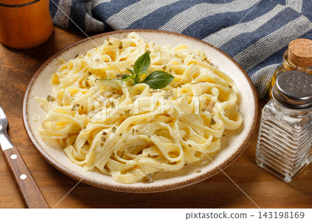 Fettuccine pasta in a white cheese sauce, served on a rustic plate with fresh basil on a wooden table. Fettuccine pasta in a white cheese sauce, served on a rustic plate with fresh basil on a wooden table. 143198169