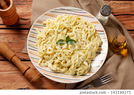 Traditional Fettuccine Alfredo with creamy white sauce on a ceramic plate, finished with green basil, on a wooden table Traditional Fettuccine Alfredo with creamy white sauce on a ceramic plate, finished with green basil, on a wooden table 143198173