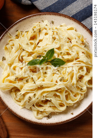 Fettuccine Alfredo with cheese sauce on a rustic plate, accompanied by fresh basil, on a rustic table. Fettuccine Alfredo with cheese sauce on a rustic plate, accompanied by fresh basil, on a rustic table. 143198174