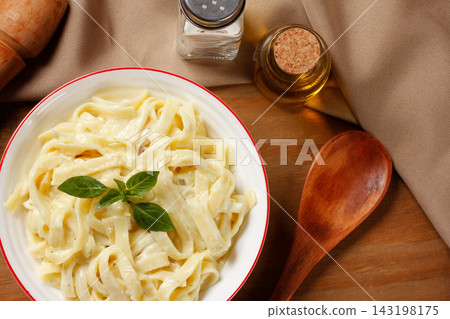 Creamy Fettuccine Alfredo with cheese sauce, served in a white bowl with fresh basil on a wooden table. 143198175