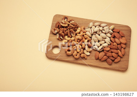 Mix of various nuts on cutting board on beige background. Pistachios, cashews, walnuts, hazelnuts, peanuts. 143198627