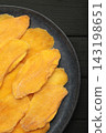 Slices of dried mango on dark plate on black background. Vertical photo 143198651
