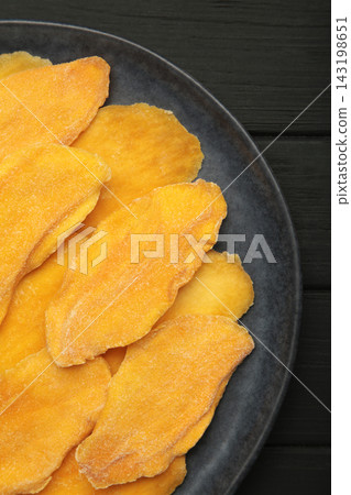 Slices of dried mango on dark plate on black background. Vertical photo Slices of dried mango on dark plate on black background. Vertical photo 143198651