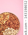 Mix of various nuts on plate on pink background. Pistachios, cashews, walnuts, hazelnuts, peanuts. Vertical photo 143198652