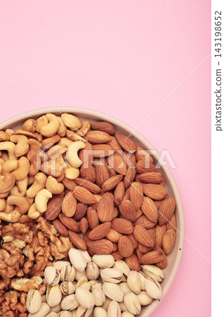 Mix of various nuts on plate on pink background. Pistachios, cashews, walnuts, hazelnuts, peanuts. Vertical photo 143198652