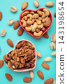 Mixed nuts on a heart-shaped plate on blue background. Almonds, pistachio, walnuts, cashew, hazelnut. Vertical photo 143198654