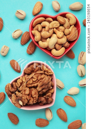 Mixed nuts on a heart-shaped plate on blue background. Almonds, pistachio, walnuts, cashew, hazelnut. Vertical photo 143198654