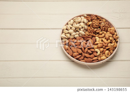 Mix of various nuts on plate on light background. Pistachios, cashews, walnuts, hazelnuts, peanuts. Space for text 143198655