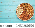 Mix of various nuts on plate on blue background. Pistachios, cashews, walnuts, hazelnuts, peanuts. Space for text 143198659