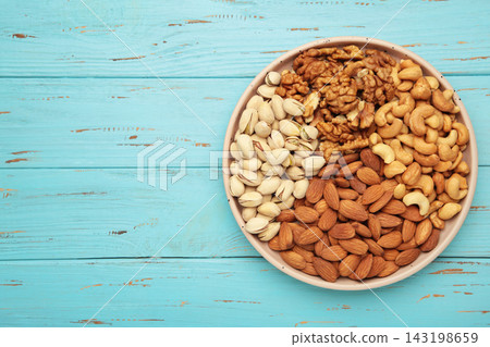 Mix of various nuts on plate on blue background. Pistachios, cashews, walnuts, hazelnuts, peanuts. Space for text 143198659