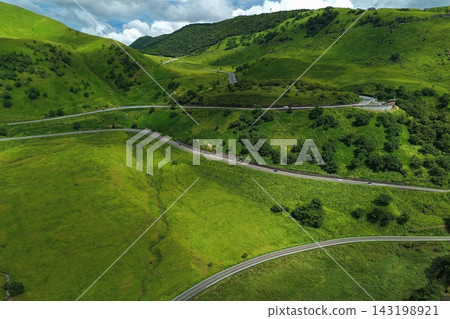 一張空拍照片,展現了大分縣由布市的草原和蜿蜒的道路。 一張空拍照片,展現了大分縣由布市的草原和蜿蜒的道路。 143198921