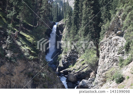 Mountain Waterfall in Kyrgyzstan Surrounded by Coniferous Forest and Rocky Mountains Mountain Waterfall in Kyrgyzstan Surrounded by Coniferous Forest and Rocky Mountains 143199098