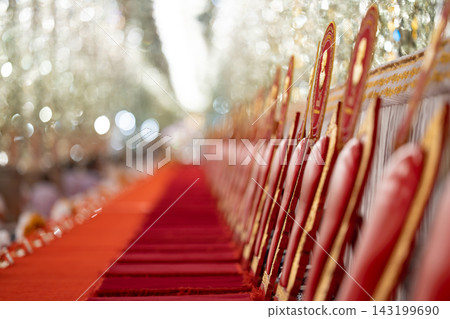 A long row of red ceremonial cushions and golden fans for Buddhist monks rests on a platform against a sparkling blurred A long row of red ceremonial cushions and golden fans for Buddhist monks rests on a platform against a sparkling blurred 143199690