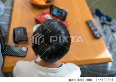 The back view of a 13-year-old boy sitting at a kotatsu (heated table). The back view of a 13-year-old boy sitting at a kotatsu (heated table). 143199871
