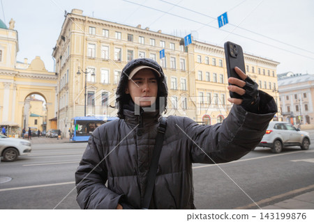 Young man taking selfie with smartphone on city street in winter. Urban tourist photography and social media lifestyle concept. Travel blogger creating content outdoors Young man taking selfie with smartphone on city street in winter. Urban tourist photography and social media lifestyle concept. Travel blogger creating content outdoors 143199876