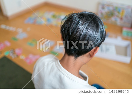 從背後拍攝到一名 13 歲男孩獨自坐在地板上玩棋盤遊戲。 143199945