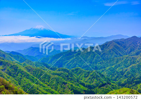 A wide-angle shot of the majestic, snow-capped Mt. Fuji and the surrounding Tanzawa mountain range, taken from the summit plaza of Mt. Tōnodake in early summer, under a clear blue sky. A wide-angle shot of the majestic, snow-capped Mt. Fuji and the surrounding Tanzawa mountain range, taken from the summit plaza of Mt. Tōnodake in early summer, under a clear blue sky. 143200572