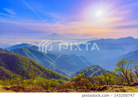 A wide-angle shot taken from the summit of Mt. Tōnodake in the Tanzawa Mountains in early summer, capturing the beautiful sunset shining in the evening sky and the majestic silhouette of Mt. Fuji. A wide-angle shot taken from the summit of Mt. Tōnodake in the Tanzawa Mountains in early summer, capturing the beautiful sunset shining in the evening sky and the majestic silhouette of Mt. Fuji. 143200747