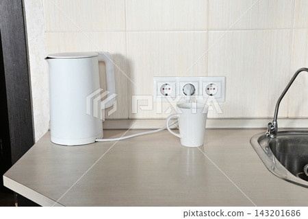 Electric kettle and mug on kitchen counter by sink Electric kettle and mug on kitchen counter by sink 143201686