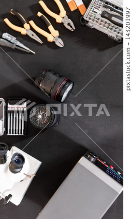 Top view of a black workbench with hand tools, camera lens, compass, microscope, electronic parts and a drawing tablet for creative repair work. Top view of a black workbench with hand tools, camera lens, compass, microscope, electronic parts and a drawing tablet for creative repair work. 143201997