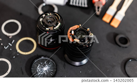 Top view of disassembled camera lenses, lens parts and small repair tools on a dark work surface, camera maintenance and optical equipment service. Top view of disassembled camera lenses, lens parts and small repair tools on a dark work surface, camera maintenance and optical equipment service. 143202005