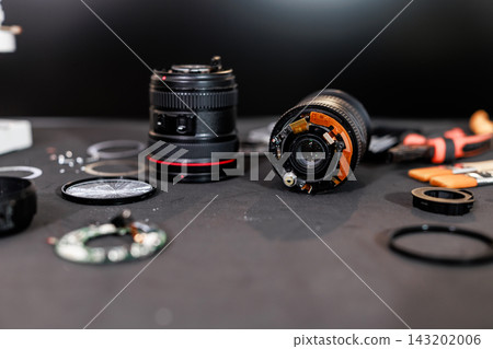 Close-up of disassembled camera lenses and small repair parts on a dark workbench, maintenance, optical equipment repair and photography technology. 143202006