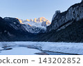 Cinematic sunset over Alpine lake in winter mountains. Winter mountain landscape. Golden hour reflection in calm mountain lake. Alpine peaks illuminated by orange light of setting sun. 143202852