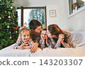 Happy family in festive pajamas hugging on bed on Christmas Eve in decorated apartment. Dad, mom,daughter, son are lying on bed and having fun together. Family celebrating winter holidays at home 143203307