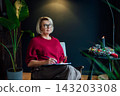 Middle aged woman planning goals for next new year while sitting on armchair in cozy dark home interior. Self-reflection concept. Personal Year review. Coaching tools. Finding Balance in Life. 143203308