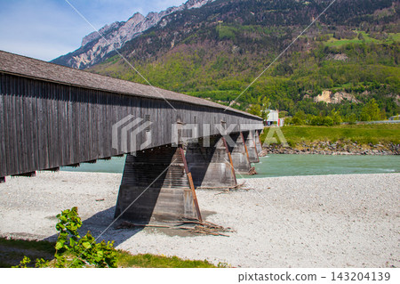Covered wooden old bridge (Alte Rheinbrucke) the across the river Rhine between Vaduz, Liechtenstein and Sevelen, Switzerland Covered wooden old bridge (Alte Rheinbrucke) the across the river Rhine between Vaduz, Liechtenstein and Sevelen, Switzerland 143204139