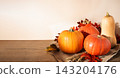 Assorted pumpkins and butternut squash on burlap with fall leaves and wheat over wooden table. Autumn harvest background with copy space on left for Thanksgiving and seasonal promotions. 143204176