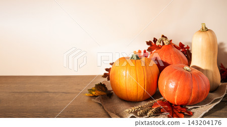 Assorted pumpkins and butternut squash on burlap with fall leaves and wheat over wooden table. Autumn harvest background with copy space on left for Thanksgiving and seasonal promotions. Assorted pumpkins and butternut squash on burlap with fall leaves and wheat over wooden table. Autumn harvest background with copy space on left for Thanksgiving and seasonal promotions. 143204176
