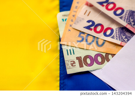 Ukrainian money and hryvnia banknotes in an envelope on blue and yellow flag background Ukrainian money and hryvnia banknotes in an envelope on blue and yellow flag background 143204394