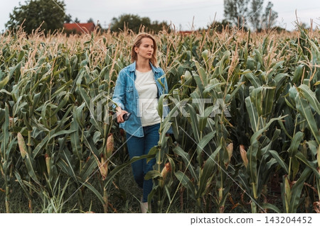 Female farmer walking and inspecting cornfield plantation Female farmer walking and inspecting cornfield plantation 143204452