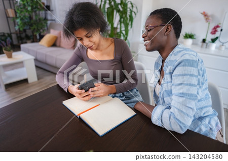 Two Young Women Using Mobile Phone and Notebook at Home Two Young Women Using Mobile Phone and Notebook at Home 143204580