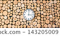 Clock on wood logs creates a timber wall background with wooden texture and rustic decor. Analog timepiece among natural tree cuts suits time planning, forestry, woodworking themes, sustainable 143205009