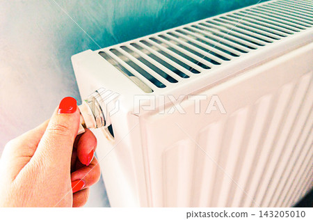 Woman adjusts radiator thermostat for home heating, temperature control, warmth and energy saving during cold winter season. Hand turns valve on white radiator to regulate indoor heat, reduce energy Woman adjusts radiator thermostat for home heating, temperature control, warmth and energy saving during cold winter season. Hand turns valve on white radiator to regulate indoor heat, reduce energy 143205010