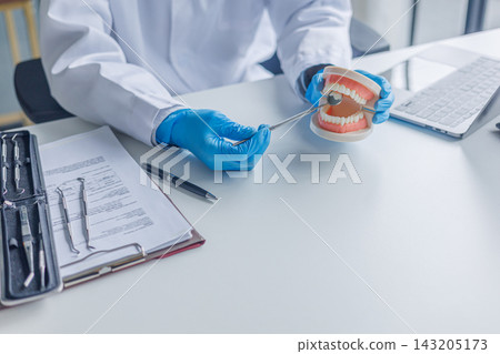 A dentist explains the process using a physical denture model to show patients how the treatment is planned A dentist explains the process using a physical denture model to show patients how the treatment is planned 143205173