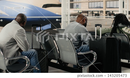 Multiracial people sitting on chairs in busy airport terminal talking, waiting to catch plane. Diverse passengers on metal benches chatting before boarding departure gate opens Multiracial people sitting on chairs in busy airport terminal talking, waiting to catch plane. Diverse passengers on metal benches chatting before boarding departure gate opens 143205473