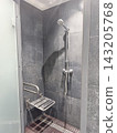Accessible shower bathroom has disability seat, grab bars, mixer and handheld shower for hygiene. Medical center plumbing installation, accessible sanitation, mobility support, safety shower fixtures. 143205768