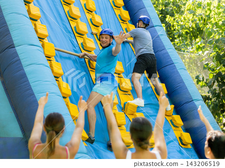 Men using sticks to reach top of slide in adventure park Men using sticks to reach top of slide in adventure park 143206519